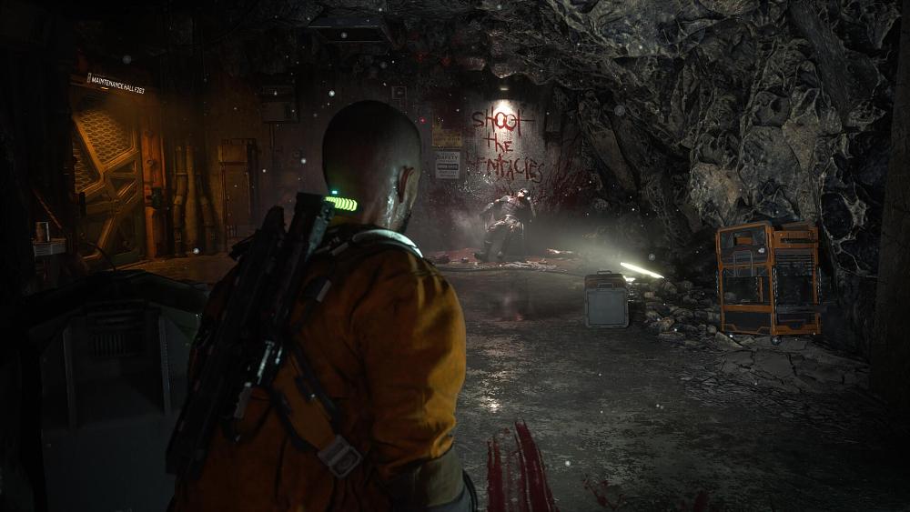 Bald man in an orange prison jumpsuit standing in a grotesque environment where there is slime and other organic material covering the walls.