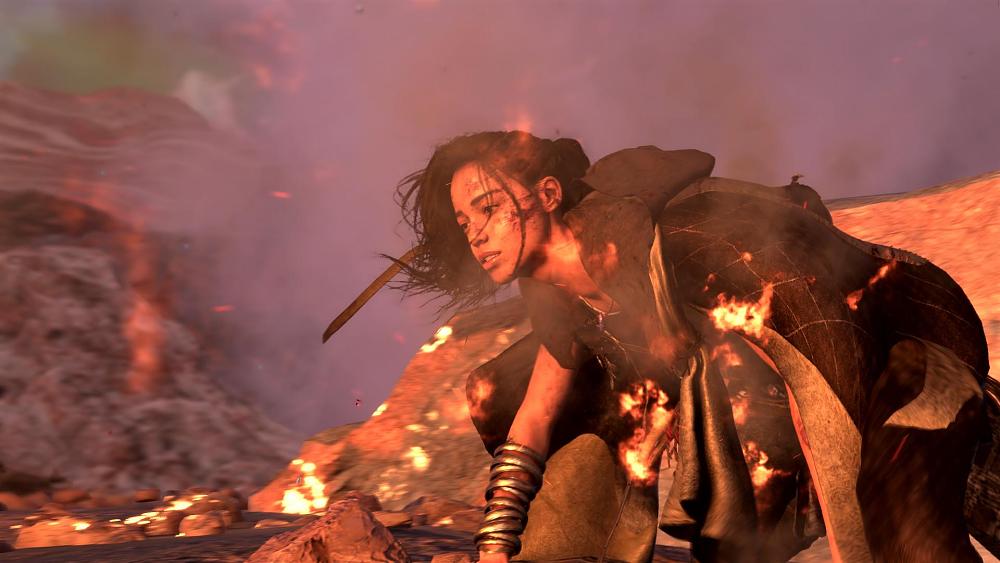 Image of a young, Black woman wearing several bracelets on one arm and what looks like a black cloak. She seems to be kneeling on the ground, struggling to stand up and is apparently surrounded by a few embers. She looks a bit pained and has what appears to be blood on her face.