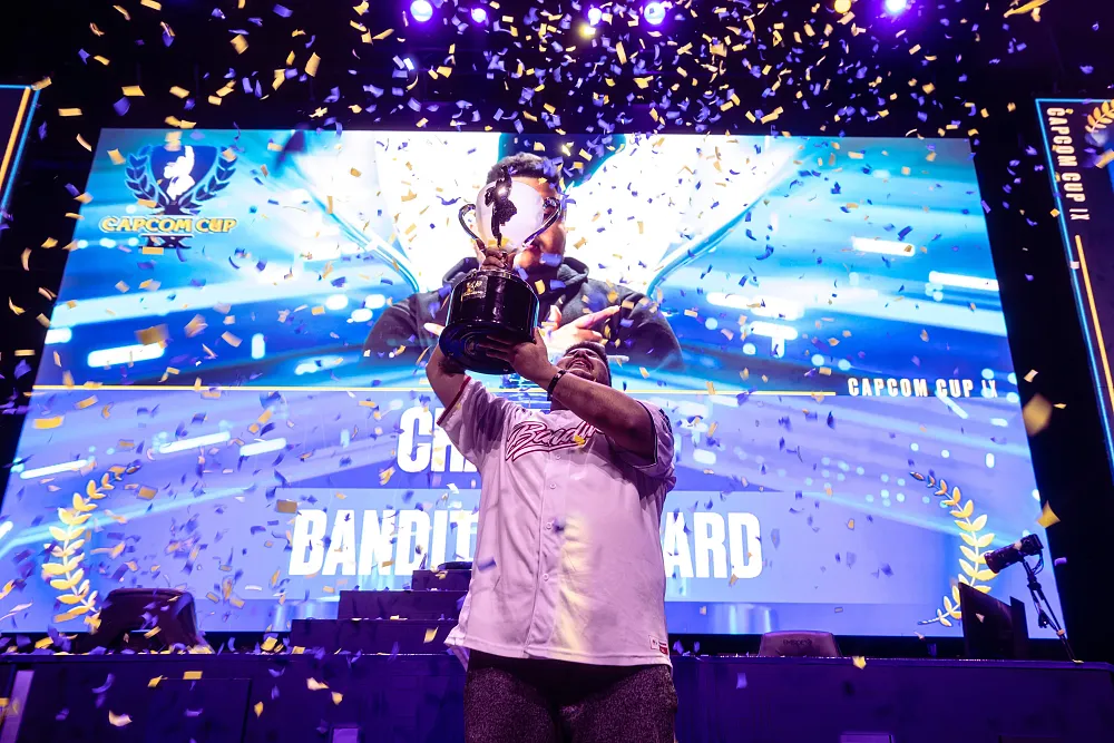 An eSports player hoisting a large trophy above his head as confetti falls down around him.