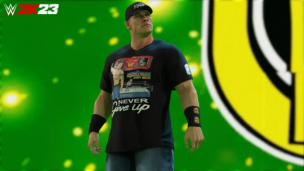 A muscular wrestler in jorts, a black shirt, and black baseball cap poses in front of a large screen.