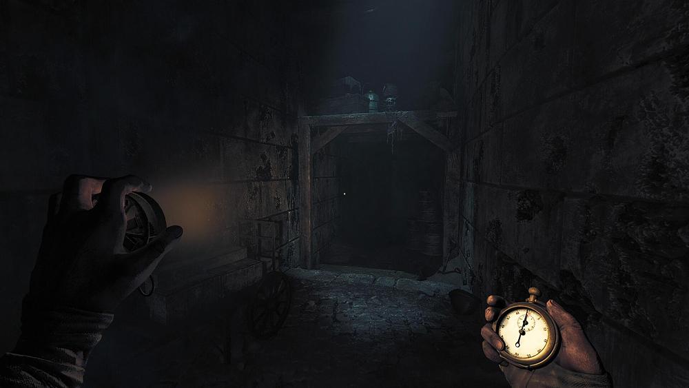 First person view holding up a light in one hand and a timer in the other, standing in a dark and rocky corridor.