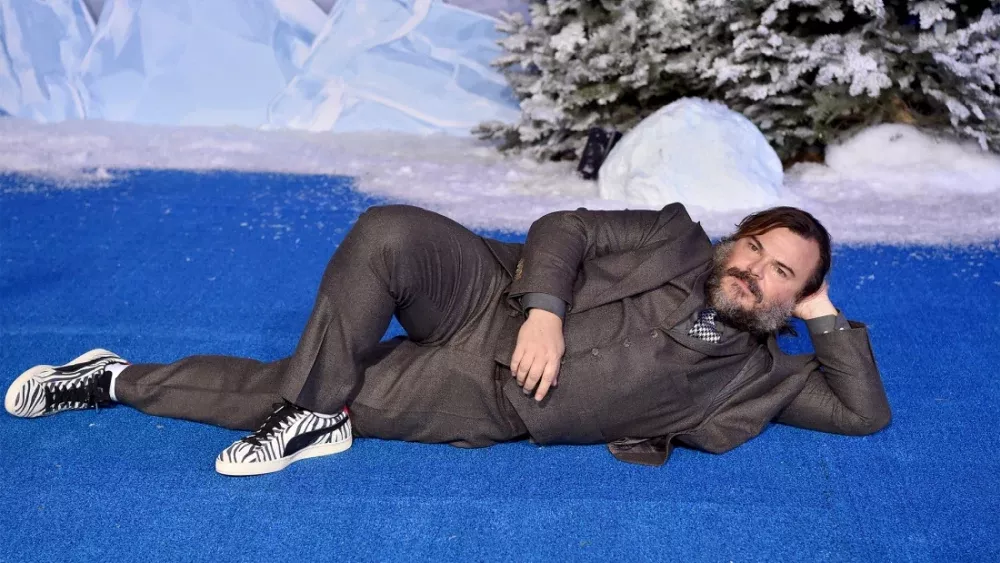 Actor Jack Black in a suit laying in a seductive pose on a blue carpet.