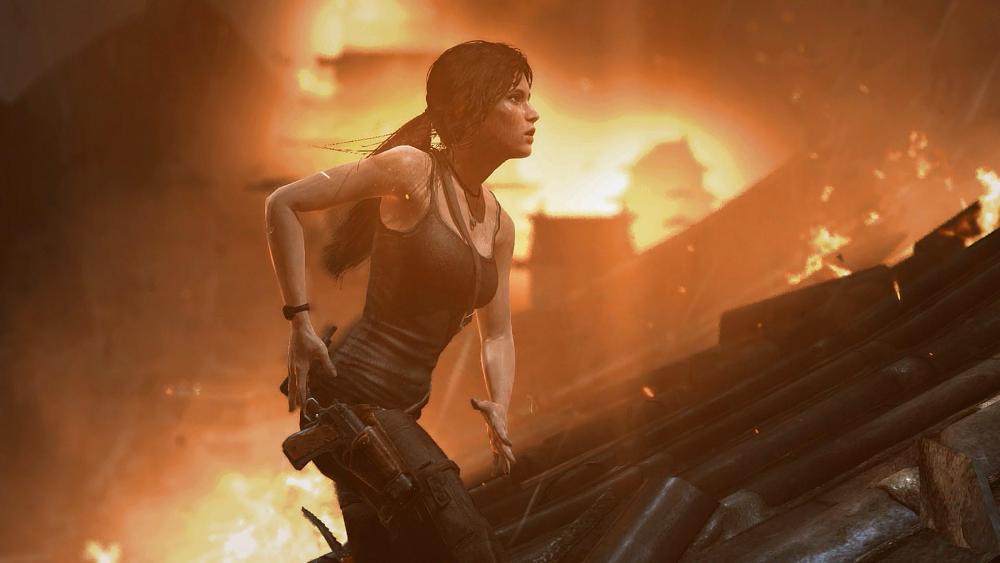 Young Lara Croft reaching for a gun as a fire rages around her and in the background.